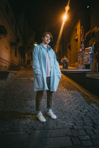 Portrait of teenage girl standing on footpath at night