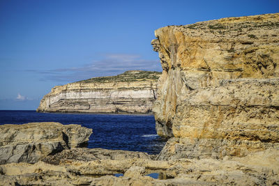 Rock formations by sea against blue sky