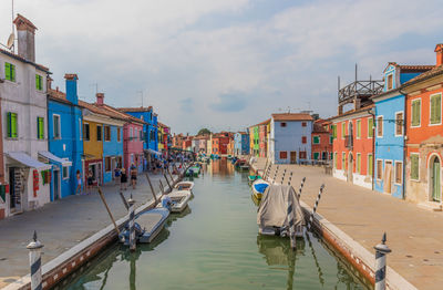 Boats moored in canal amidst buildings against sky