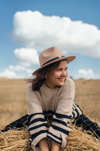 Portrait of smiling young woman wearing hat on field against sky