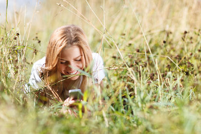 Smiling young woman using mobile phone while lying on grass