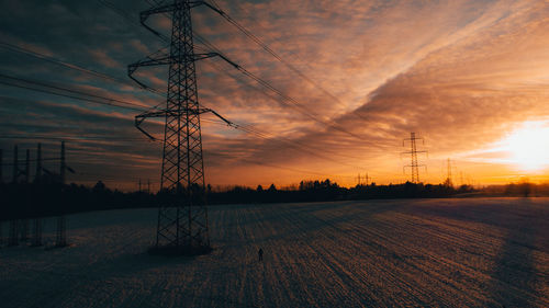 Electricity pylon on field against romantic sky at sunset