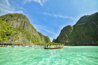 Boats on sea by mountain against sky