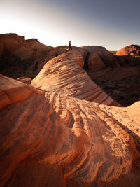 Distant view of young man standing on rock formation against sky