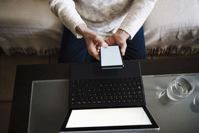 Senior woman with laptop using mobile phone while sitting on sofa at home