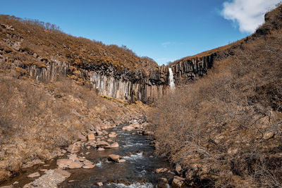 Idyllic svartifoss waterfall amidst basalt columns and stream against blue sky