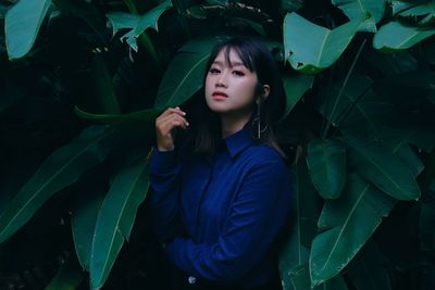 Portrait of young woman standing against leaves