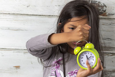 Girl holding alarm clock against wall