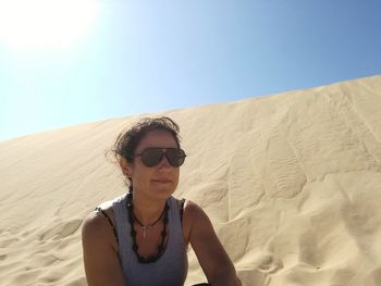 Young woman wearing sunglasses standing on sand dune against clear sky