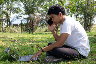 Side view of young man using mobile phone in field