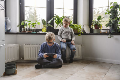 Boy sitting on radiator with brother using smart phone at home