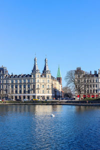 Buildings by river against clear blue sky