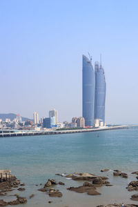 Sea by cityscape against clear blue sky