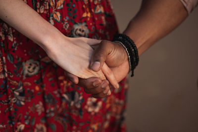Crop anonymous woman in colorful dress and black man with bracelet on wrist holding hands while enjoying romantic moments together
