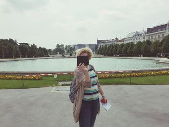 Woman photographing through mobile phone on street against pond