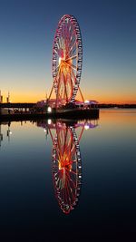 Illuminated ferris wheel against sky at sunset