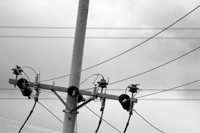 Low angle view of birds perching on cable against sky