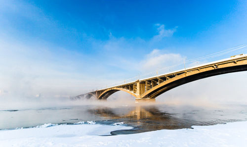 Low angle view of bridge over yenisei river against blue sky on sunny day