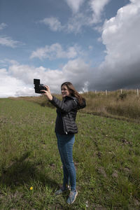 Woman blogger filming herself with her camera in her hand happy posing in the middle of the field