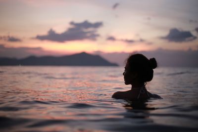 Woman swimming in sea against sky during sunset