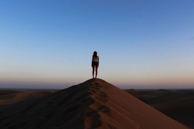 Full length of woman standing on sand dune against sky during sunset