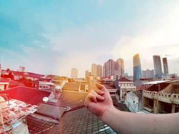 Cropped hand showing middle finger against sky in cityscape