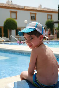 Portrait of shirtless boy sitting on pool side on sunny day