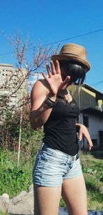 Low section of woman standing by plants against blue sky