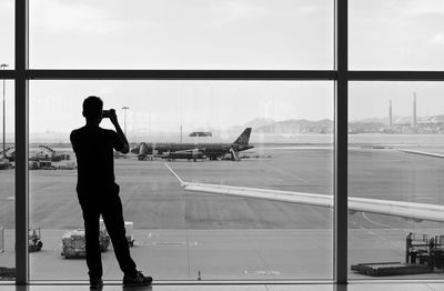 Rear view of silhouette man photographing against window at airport