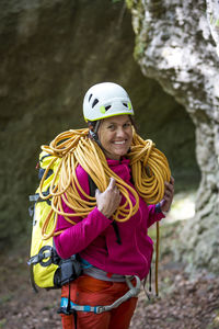 Portrait of happy woman carrying rope while standing against rocks