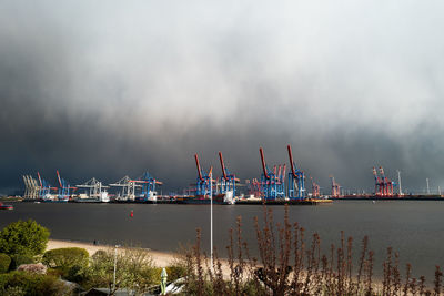 Cranes at harbor against sky