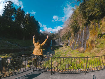 Rear view of woman with arms outstretched against plants