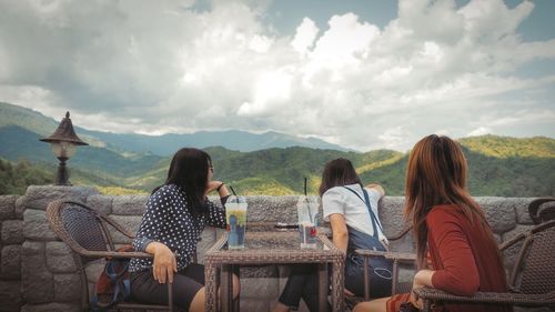 Friends sitting at cafe on mountain against cloudy sky