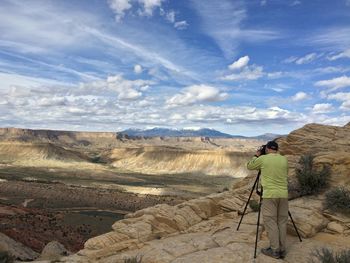 Rear view of man photographing desert against cloudy sky