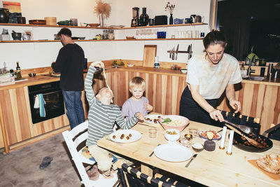 Brothers enjoying dinner at dining table with mother in kitchen