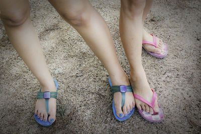 Low section of friends wearing flip-flops standing on sand at beach