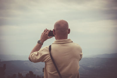 Rear view of man photographing while standing against mountains