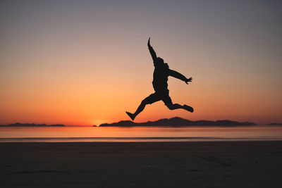 Silhouette man jumping at beach against sky during sunset