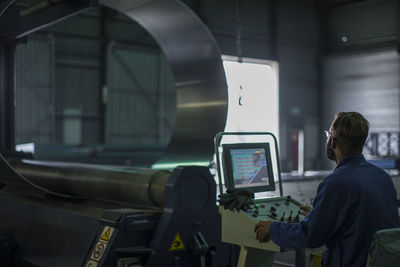 Worker operating machinery at control panel in steel factory