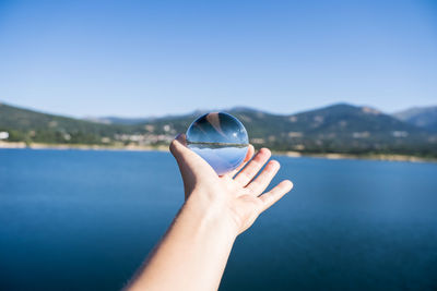 Cropped image of hand holding crystal ball against blue sky