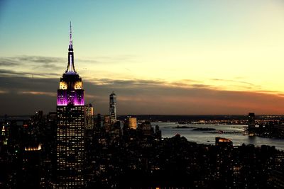 Illuminated city at waterfront during sunset