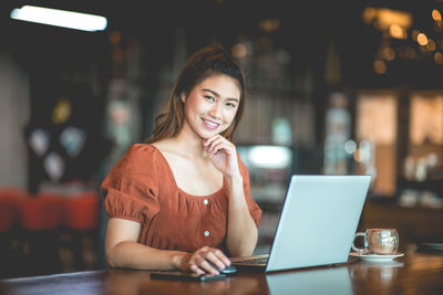 Portrait of smiling woman using laptop in cafe