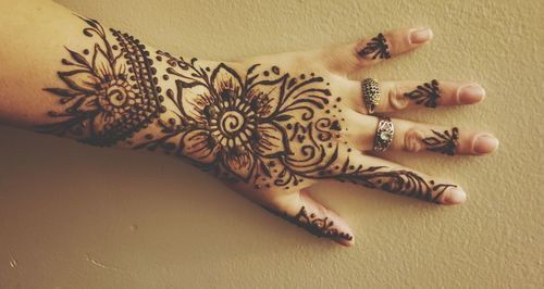 Cropped hand with henna tattoo on yellow wall