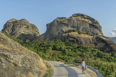 Rear view of woman walking with dog on street against mountains