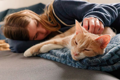 A young adolescent girl lying on a couch finds comfort by snuggling and petting her tabby cat