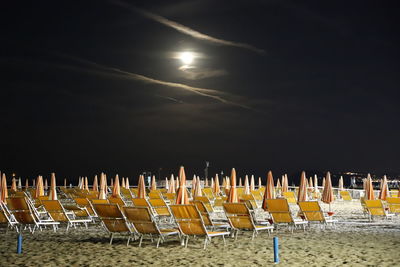 Chairs on beach against sky at night