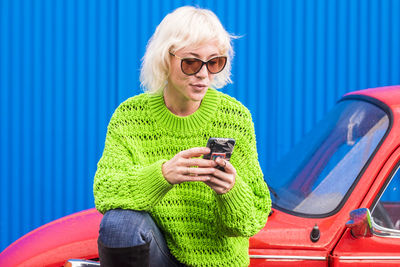 Smiling woman using mobile phone while sitting on car