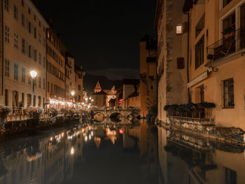 Illuminated buildings by canal in city at night