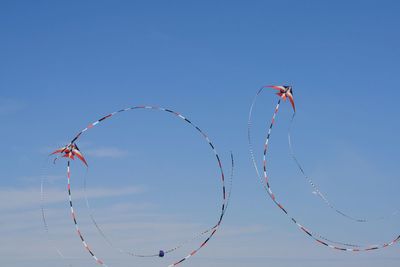 Low angle view of kites flying against clear blue sky