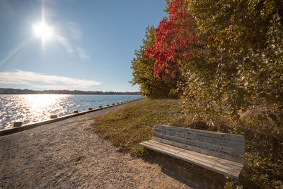 Bench by lake against sky